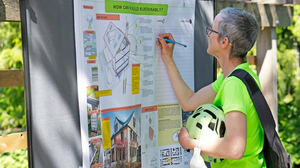 A person writes on a poster while holding a soccer ball, surrounded by greenery.