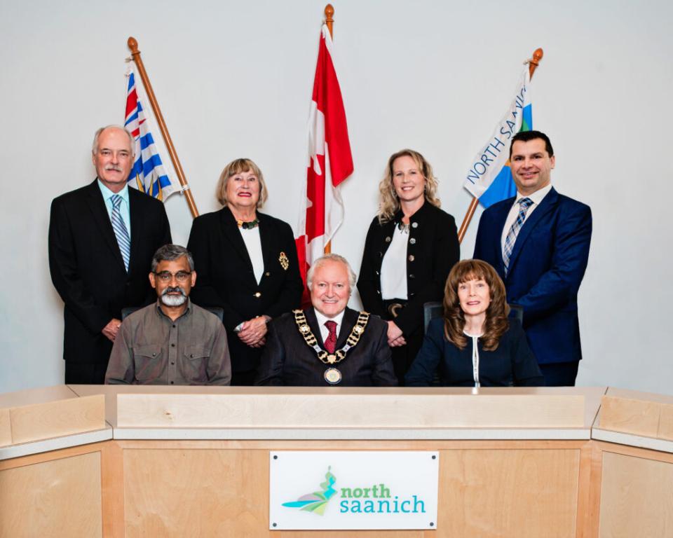 A group of officials poses at a conference table with flags behind them, smiling.