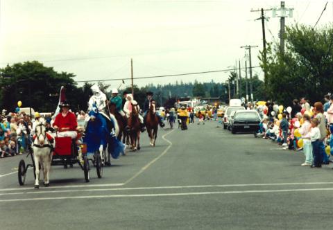 Horses and riders follow behind a horse and cart as they walk along a main street for the parade.