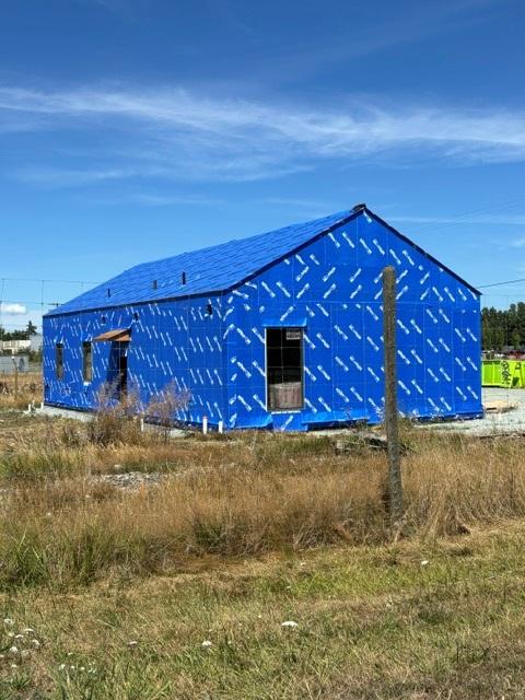 The back of an unfinished rectangular building with its exterior wrapped in blue housewrap.